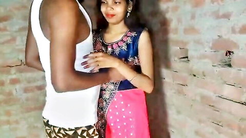 Dark-skinned man embracing Indian woman in embroidered dress against wall