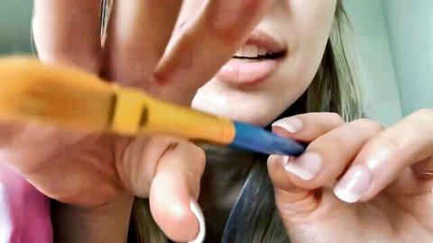 Asian woman teases mouth with yellow-blue pen in close-up ASMR