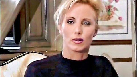 Hot blonde woman in black top, seductive expression in adult video thumbnail