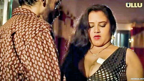 Busty Indian wife in deep cleavage black top pouting as man embraces her from behind in bedroom