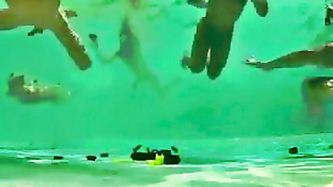 Blurry underwater shot of hands and male bodies in turquoise pool, outdoor boys fun