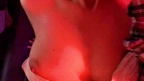 Surprised topless woman covering breasts in red-lit room
