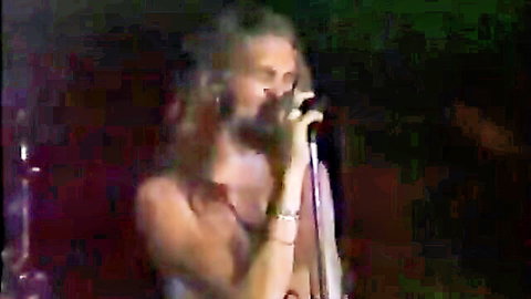 Bearded long-haired musician passionately singing on stage at local club