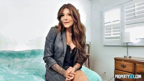 Adria Rae brunette in gray blazer and black top on bed, seductive pose