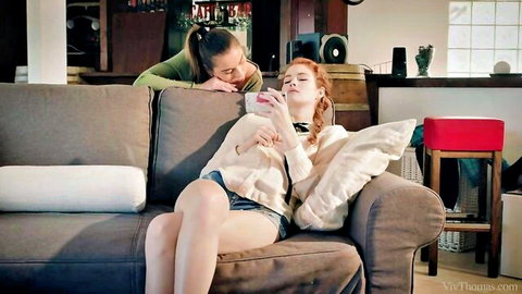 Two slim women in intimate lesbian moment, redhead lounging with phone