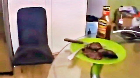Blurry closeup of grilled steaks on green plate with fork knife on glass kitchen table