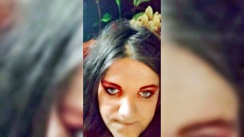 Gothic woman with intense red eyeliner and floral headpiece in bubble gum smoking fetish
