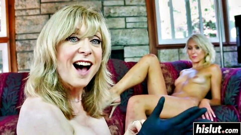 Excited topless blonde MILF smiles as gloved hand fingers nude blonde's exposed pussy on couch