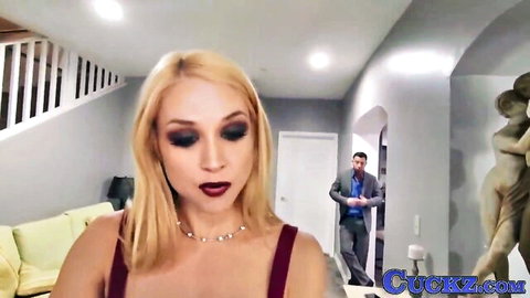 Blonde MILF in red top teases with deep cleavage while suited man watches from doorway