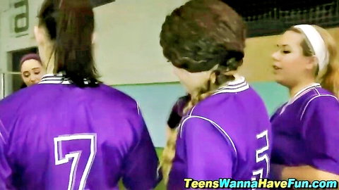 Three teen soccer girls in purple jerseys posing from behind in locker room