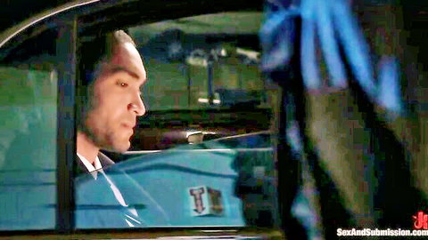 Suited man peers out car window in dimly lit BDSM domination scene