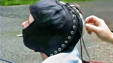 Bound woman in black leather hood and nylon costume, big hips emphasized