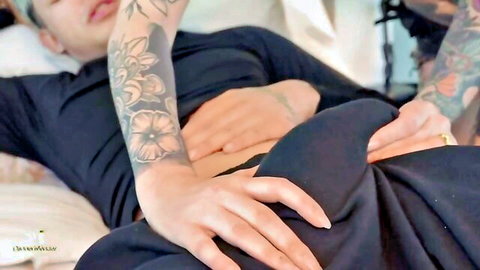 Tattooed amateur woman with floral arms grabs erect cock of lying tattooed guy on bed