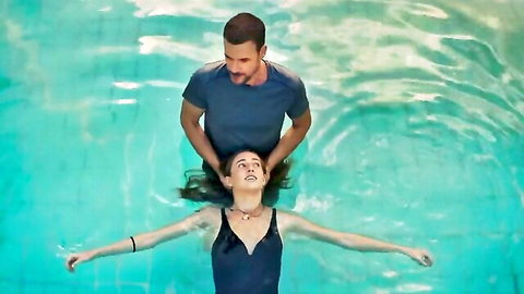 Woman in black swimsuit floating in pool, man holding hair - HIT s03 sexy celeb scene