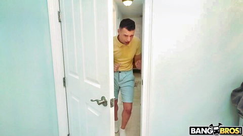 Muscular guy in yellow shirt and shorts emerging from bathroom doorway in Bang Bros scene