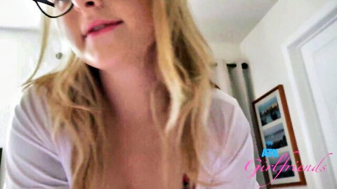 Blonde with glasses teases lips in open white top showing cleavage