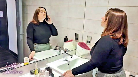 Brunette woman in black turtleneck and skirt talking on phone in bathroom mirror selfie