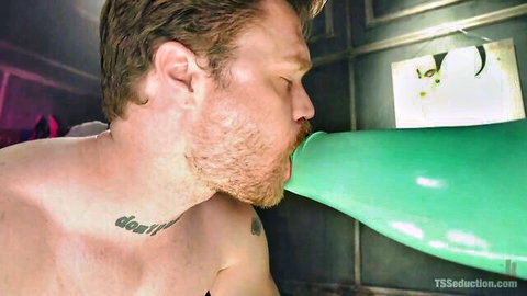 Bearded man passionately kissing huge green balloon in TS seduction fetish scene