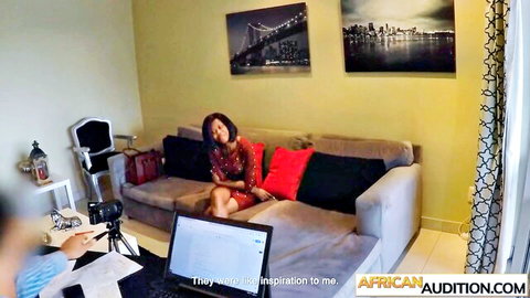 Ebony woman in tight red dress lounges smiling on couch during amateur African casting audition