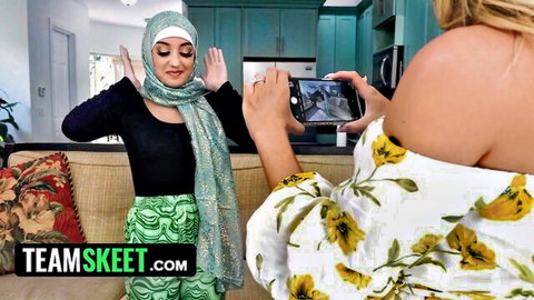 Muslim woman in hijab poses playfully as blonde friend snaps photo in kitchen
