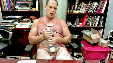 Muscular bald man in tank top holds white Hitachi wand vibrator against his small exposed cock in amateur webcam.
