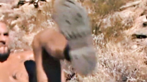 Muscular ebony hunk with beard kicks high showing boot sole outdoors in intense rough gay scene
