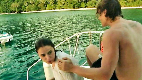 Shirtless hunk grabs brunette's wet white top at chest on yacht deck overlooking tropical ocean