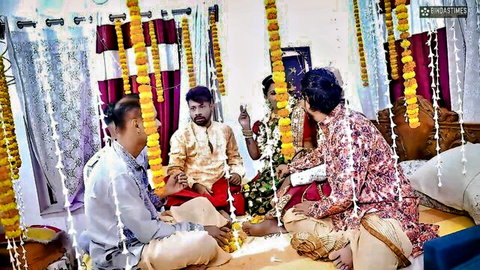 Indian bride in green saree with groom and family performing traditional wedding puja ritual surrounded by marigold garlands