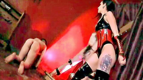 Cybill in red latex corset dominates tattooed sub in BDSM scene