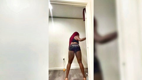 Ebony woman with red braided hair bends over in tight shorts, showcasing big ass