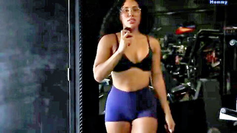 Curvy black woman in black sports bra and purple shorts, walking in gym for leg day vlog