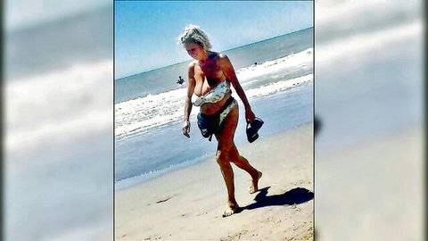 Topless busty mature granny with huge sagging tits walking barefoot on beach holding black heels
