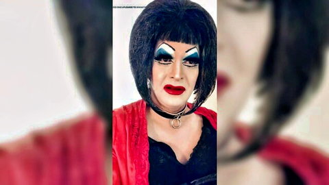 Dramatic trans sissy in black bob wig, heavy blue makeup, red lips, red robe over black lace lingerie