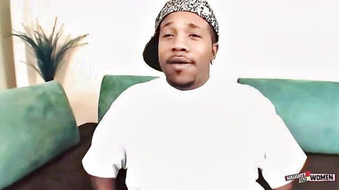 Black man in white tee and backwards cap sits on couch smirking playfully