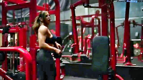 Muscular bodybuilder woman in sports bra lifting weights during arm day workout