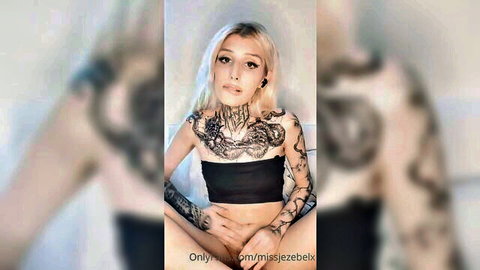 Tattooed blonde Miss Jezebel teasing crotch in black top, sensual solo vibe