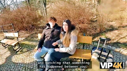 Two young women in jackets sit on outdoor bench in abandoned park, teasing lesbian encounter