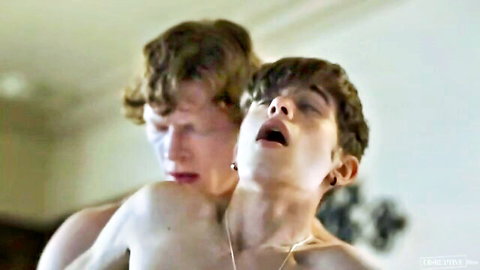 Two curly-haired young men in intense shirtless embrace during threesome play