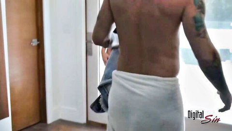 Tattooed muscular hunk in white towel holding jeans walking through doorway
