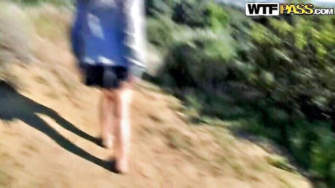 Woman in blue top and black shorts walking uphill in green park, outdoor couple sex tease