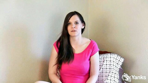 Brunette woman in pink top sits smiling in solo adult video thumbnail