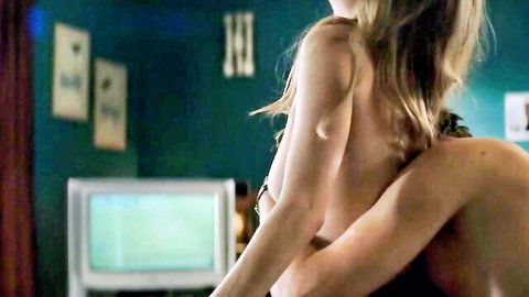 Topless blonde with bare back and sideboob embraced from behind by shirtless hunk in bedroom