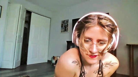 Ramona Rox camgirl in glasses and headphones, revealing black top with tattoos