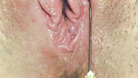 Extreme close-up of woman's clitoris with needle insertion, medical fetish focus