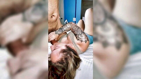 Tattooed blonde petite with small tits lying topless on bed with muscular tattooed man's arm around her