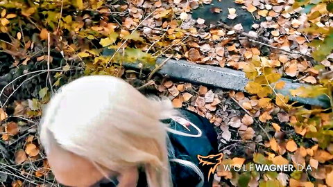 Blonde with long hair kneels nude outdoors in autumn leaves showing bare back and ass
