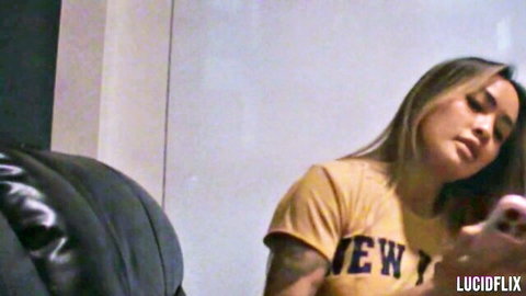 Linda Lan in yellow New York t-shirt, long hair, tattooed arm, holding phone