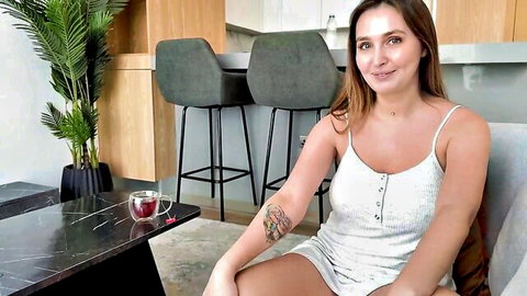Smiling brunette babe in short white slip dress teasing small tits cleavage and thighs on couch