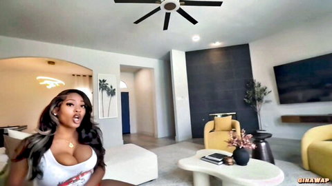 Busty ebony babe in tight white tank top flaunts massive cleavage on living room couch