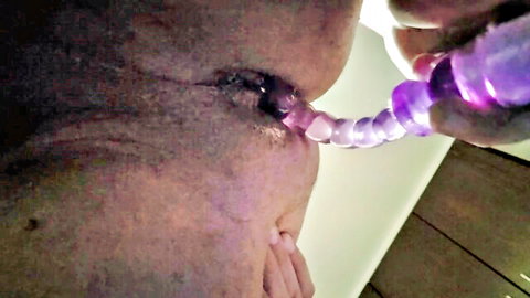 Closeup of wrinkled cock head with purple beaded urethral sound inserting into open pisshole